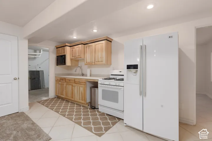Recessed lighting illuminates the kitchen area with wood cabinets, a stainless steel sink, and light-toned countertops
