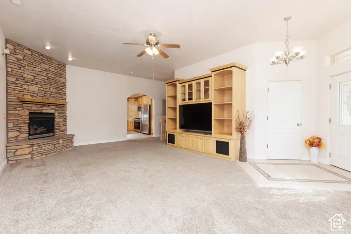 Stacked stone fireplace, built-in entertainment center, vaulted ceiling with ceiling fan, decorative entry door with leaded glass, and tiled entryway flooring