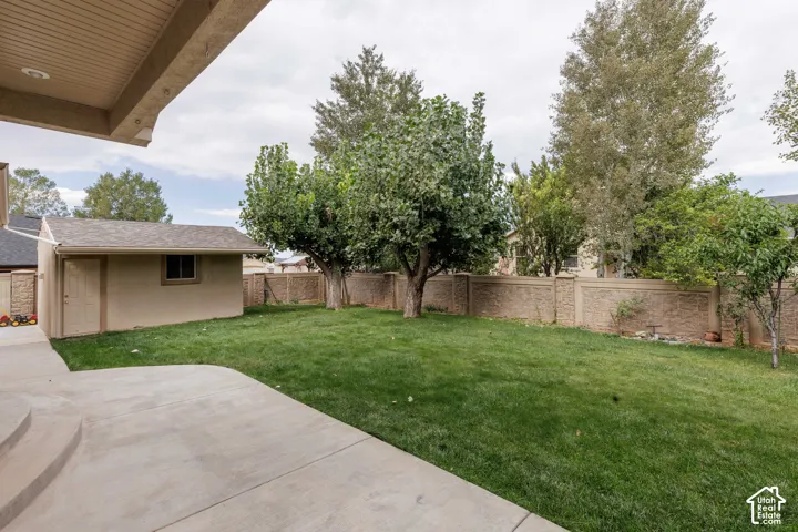 Expansive lawn with mature trees, a detached work shop/storage shed, overhead door, privacy fencing, and a concrete patio