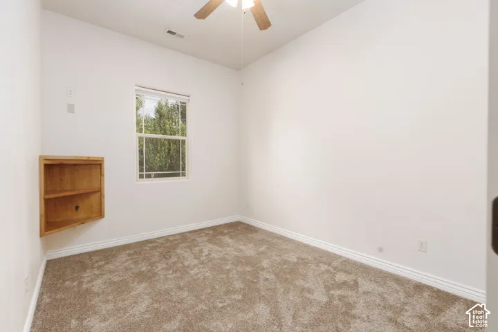 Bedroom 2 with built-in corner shelving, window with natural light, textured carpeting, ceiling fan with light fixture, and white wall finishes