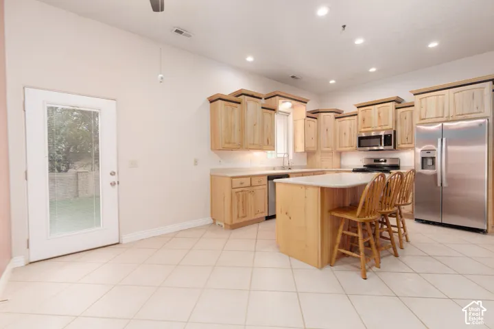 Kitchen featuring light wood cabinetry, stainless steel appliances, a center island with countertop seating, and recessed lighting