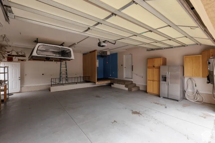 Spacious garage featuring a concrete floor, overhead garage door, built-in cabinetry, space with plumbing for hot tub and entrance to main level home
