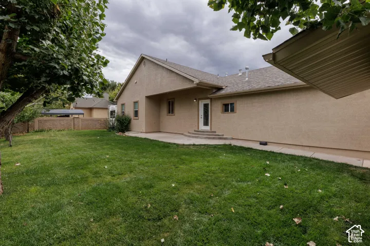 Expansive green lawn, stucco exterior, concrete patio, exterior door with glass insert, and a partial privacy fence