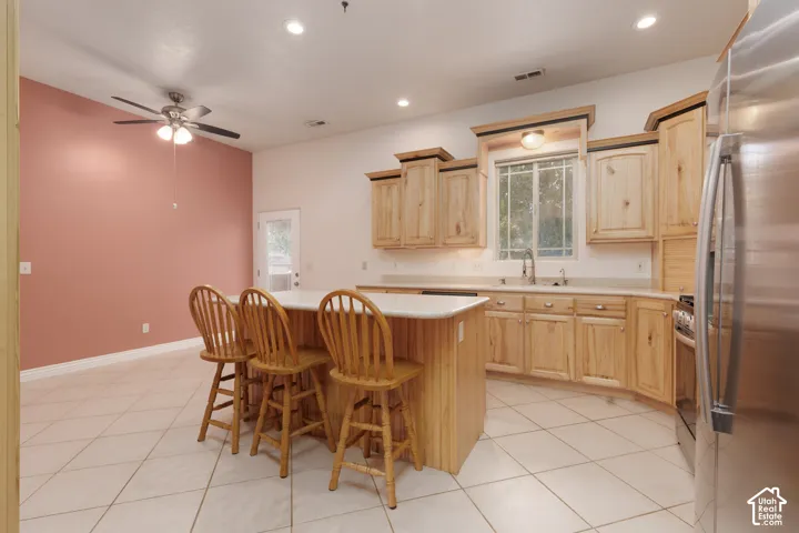 Kitchen featuring light wood cabinetry, a central island with a solid surface countertop, stainless steel refrigerator, and recessed lighting
