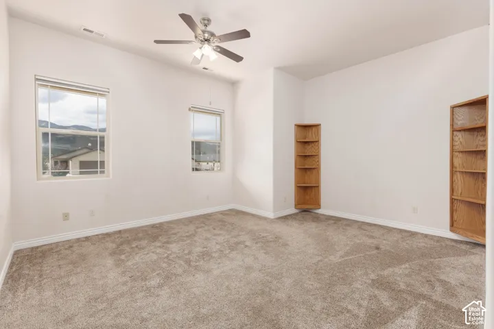 Primary bedroom with vaulted ceiling with a ceiling fan, two windows, wall-to-wall carpeting, and two built-in wooden bookshelves