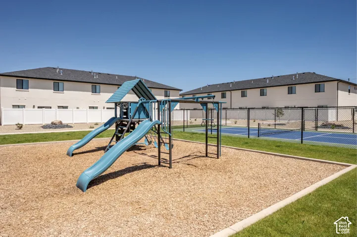 Playground area with wood chip surfacing, green lawn, a multi-level play structure with slides, and a nearby fenced court