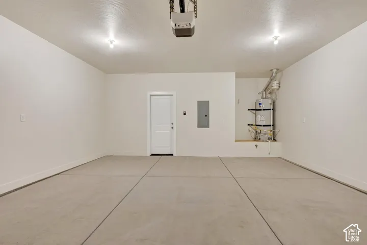 Concrete flooring, white interior door, wall-mounted electrical panel, water heater, and overhead garage door opener
