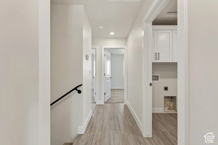 Hallway featuring wood-finish flooring, recessed lighting, white trim, and a built-in laundry area with white cabinetry