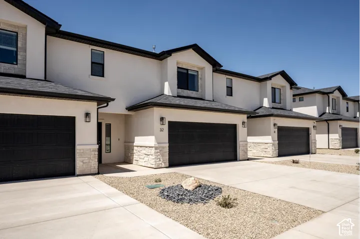 Contemporary exterior with stucco finish, stone detailing, black garage doors, and individual driveways