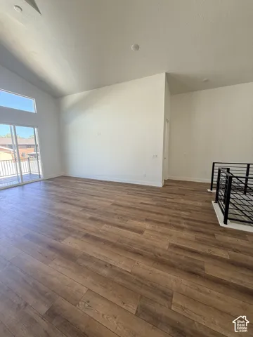Vaulted ceiling with recessed lighting, wood-finish flooring, sliding glass door, and a black metal railing