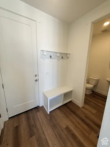 Built-in white storage bench with integrated coat hooks and shelf, white interior door, and wood-finish flooring