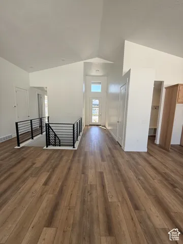 Wood-finish flooring throughout, vaulted ceiling, white walls, black metal railing, and built-in cabinetry