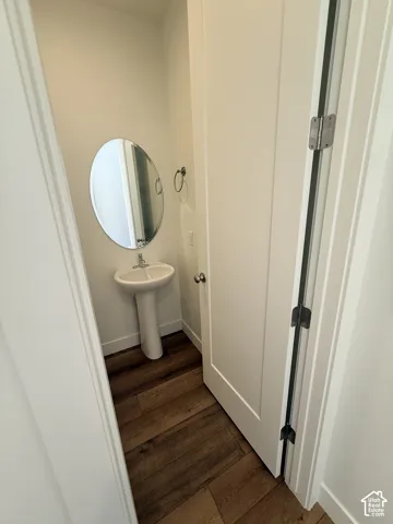 Pedestal sink with an oval mirror, wood-finish flooring, and a towel ring