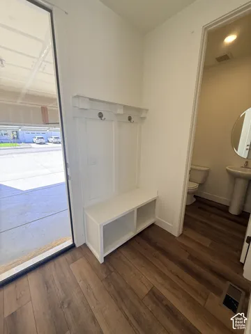 Built-in storage bench with coat hooks, wood-finish flooring, and a pedestal sink in the adjacent room