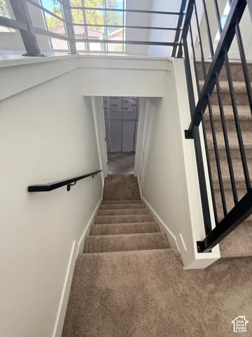 Carpeted staircase with black metal railing and white walls, leading to a lower level entry