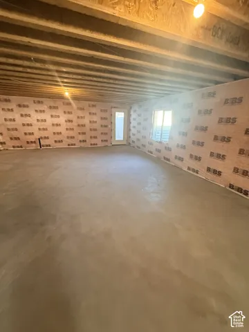 Unfinished basement featuring exposed ceiling joists, concrete flooring, exterior door, and a window