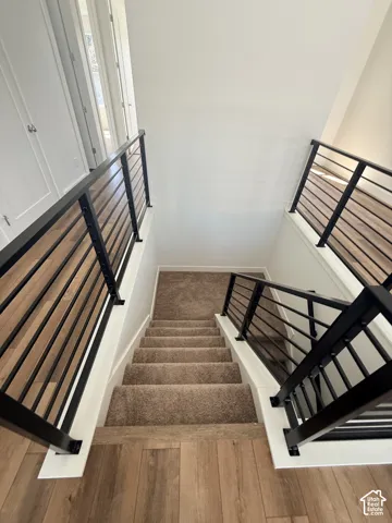 Staircase with modern black metal and wood-finish railings, carpeted treads, and wood-finish flooring