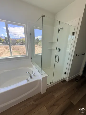 Soaking tub with chrome fixtures, glass-enclosed shower with integrated shelving, and wood-finish flooring