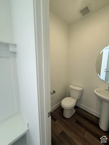 Powder room with wood-finish flooring, pedestal sink, and circular mirror