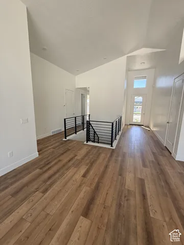 Wood-finish flooring throughout, modern black horizontal railing, white painted walls, vaulted ceilings, and a glass-paneled entry door