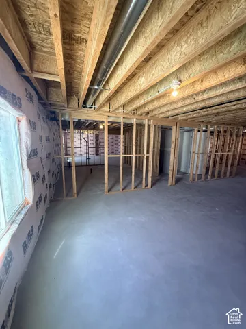 Unfinished basement featuring wood framing, exposed ceiling joists, concrete flooring, and a large window with visible insulation