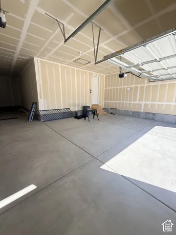 Concrete flooring, unfinished walls, ceiling with exposed framing, single entry door, and an overhead garage door