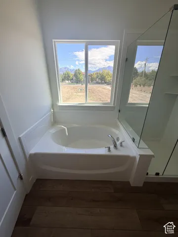 Soaking tub with a polished chrome faucet, surrounded by wood-finish flooring and a clear glass shower enclosure