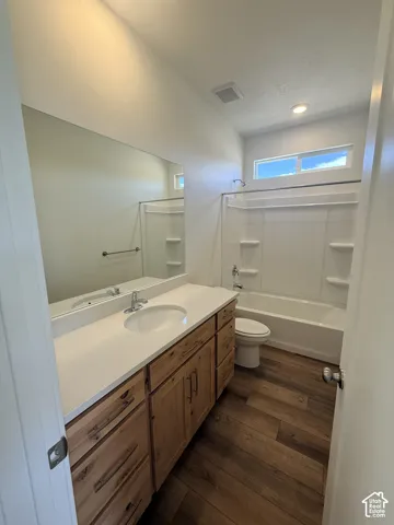 Bathroom featuring a wood-finish vanity with an integrated sink, a white countertop, and an elongated mirror