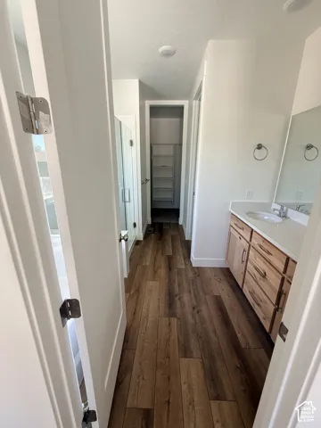 Wood-finish flooring, light wood vanity with white countertop, recessed lighting, glass-enclosed shower, and built-in closet shelving