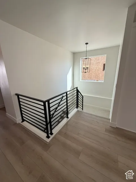 Wood-finish flooring, contemporary black metal railing, overhead chandelier, and a bright window