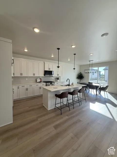 Open-concept kitchen featuring an island with built-in sink, white cabinetry, light countertops, and wood-finish flooring