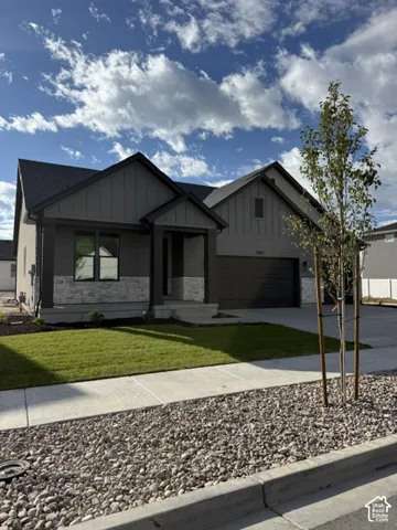 Modern exterior featuring a dark gray facade, stone accents, attached garage, covered entry, and a manicured lawn