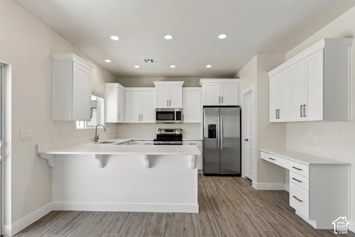 White shaker cabinetry, recessed lighting, wood-finish flooring, stainless steel appliances, and integrated desk space