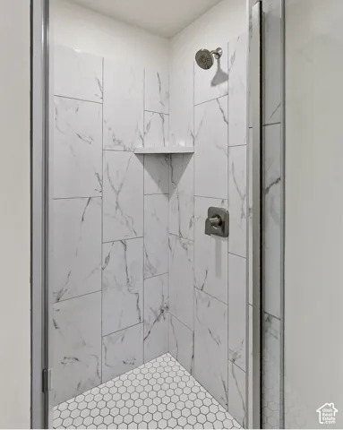 Shower stall with white marble-look wall tiles, hexagonal floor tiles, a built-in corner shelf, and brushed nickel fixtures