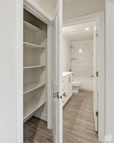 Built-in pantry shelving, wood-finish flooring, white vanity with integrated basin, white subway tile shower surround, and a white bathtub