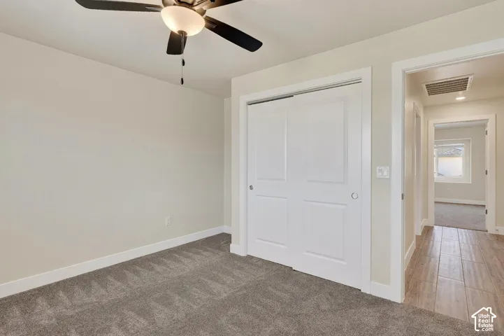 Neutral wall tones, gray carpeting, and a ceiling fan with integrated lighting