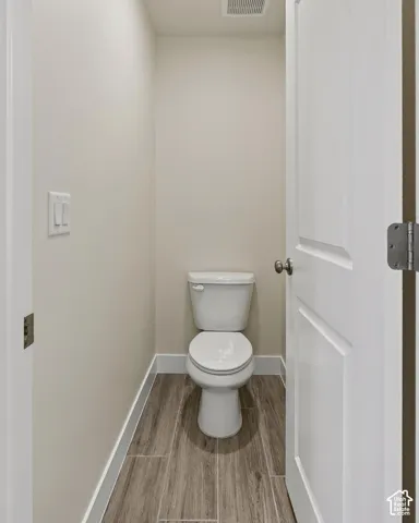 Neutral tone walls, wood-finish flooring, white door with paneling, white baseboards, and a white toilet
