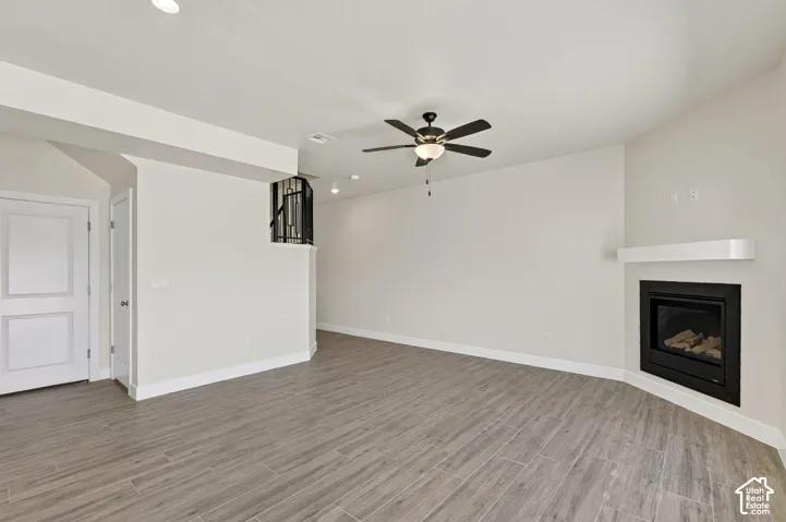 Spacious room featuring wood-finish flooring, a built-in fireplace with a white mantel, a ceiling fan with integrated lighting, and recessed lighting