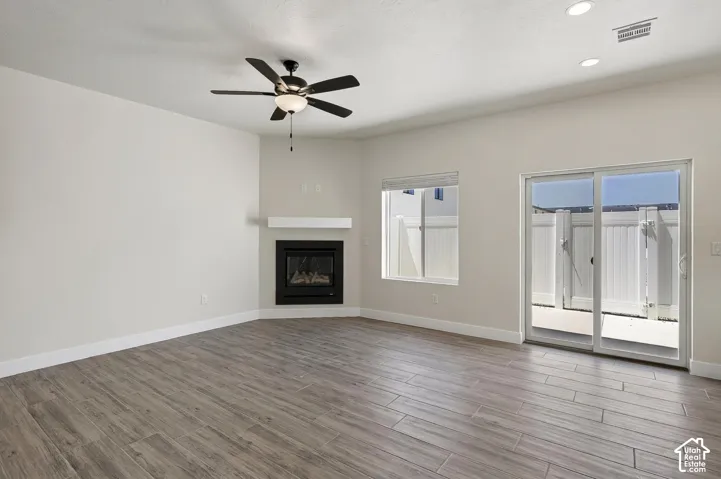 Wood-look tile flooring, corner fireplace with white mantel, ceiling fan with integrated lighting, recessed lighting, and a sliding glass door to the exterior