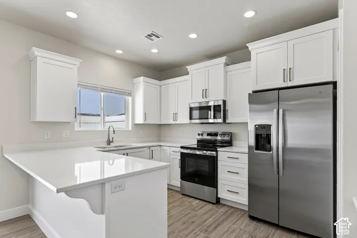 White shaker cabinetry with crown molding, stainless steel appliances, light-toned countertops, wood-finish flooring, and recessed lighting