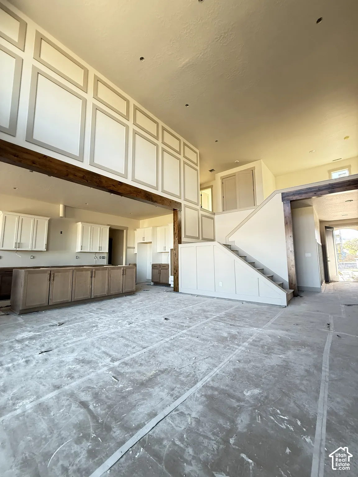 Double-height ceilings featuring decorative wall paneling, stained wood support beams, built-in cabinetry, and a staircase with wainscoting