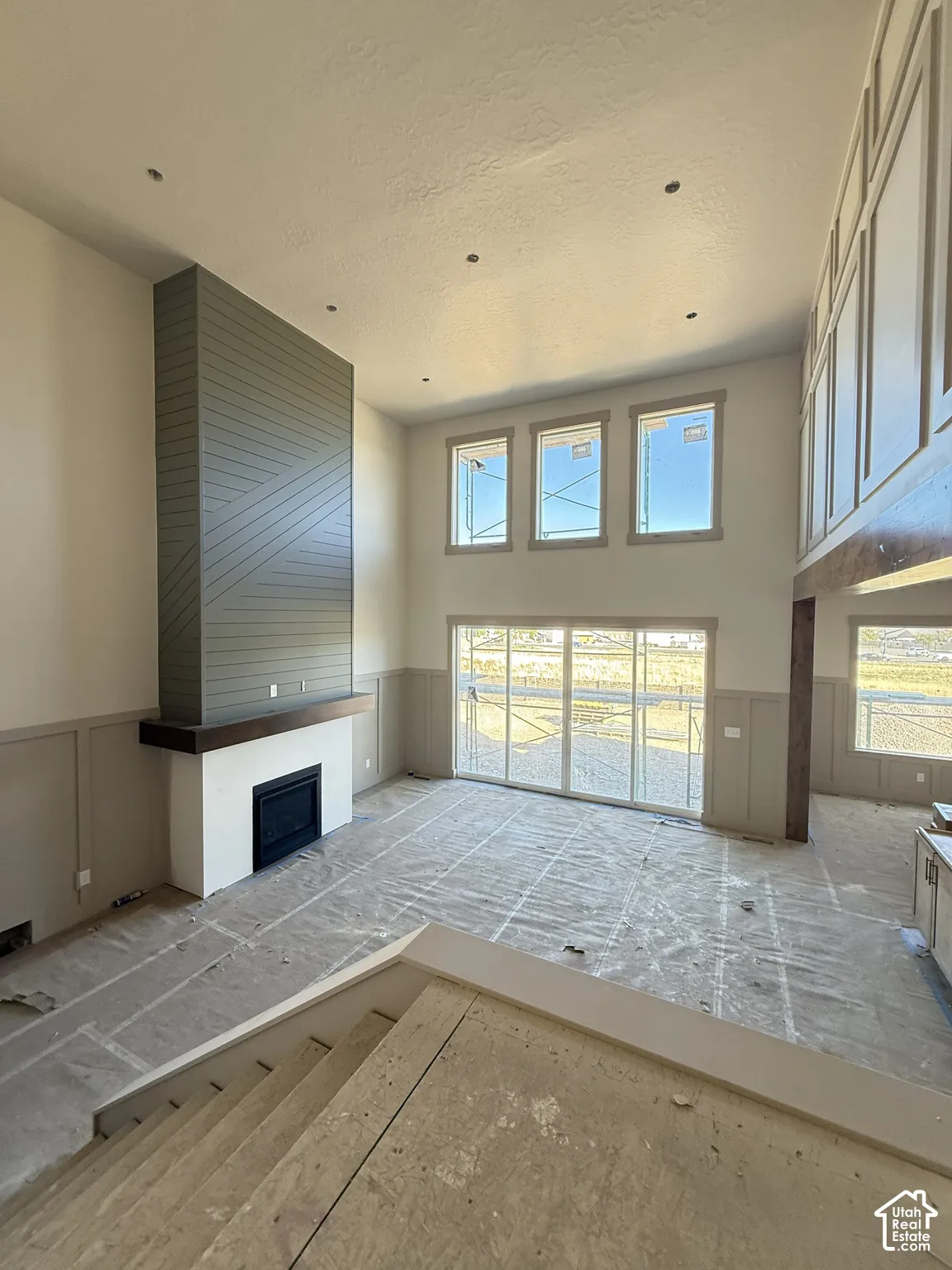 High-ceiling space featuring floor-to-ceiling fireplace surround with geometric paneling, wood-finished mantel, wainscoting, and large sliding glass doors