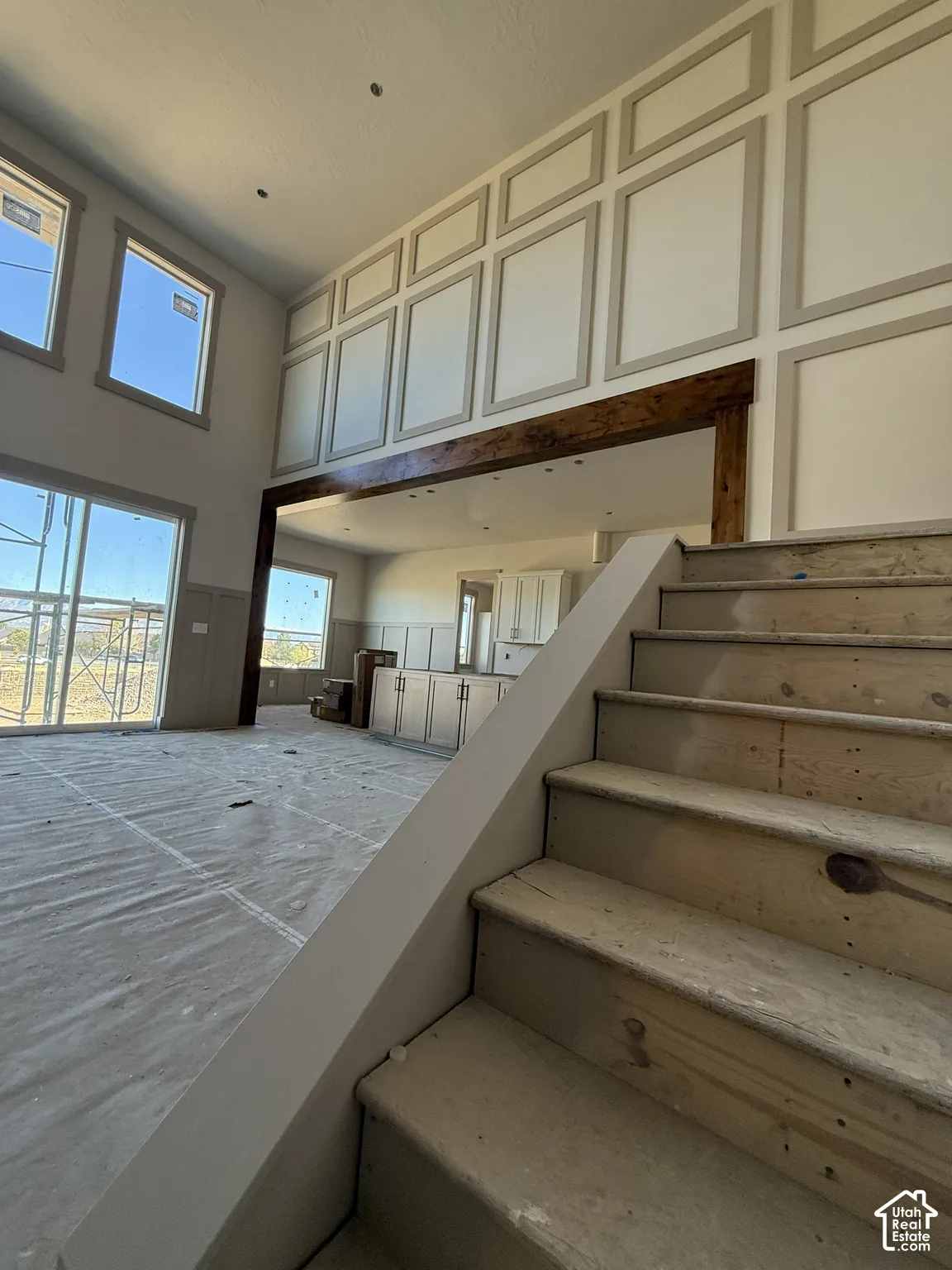Two-story ceiling with full-height wall molding, prominent natural wood support beam, and expansive windows