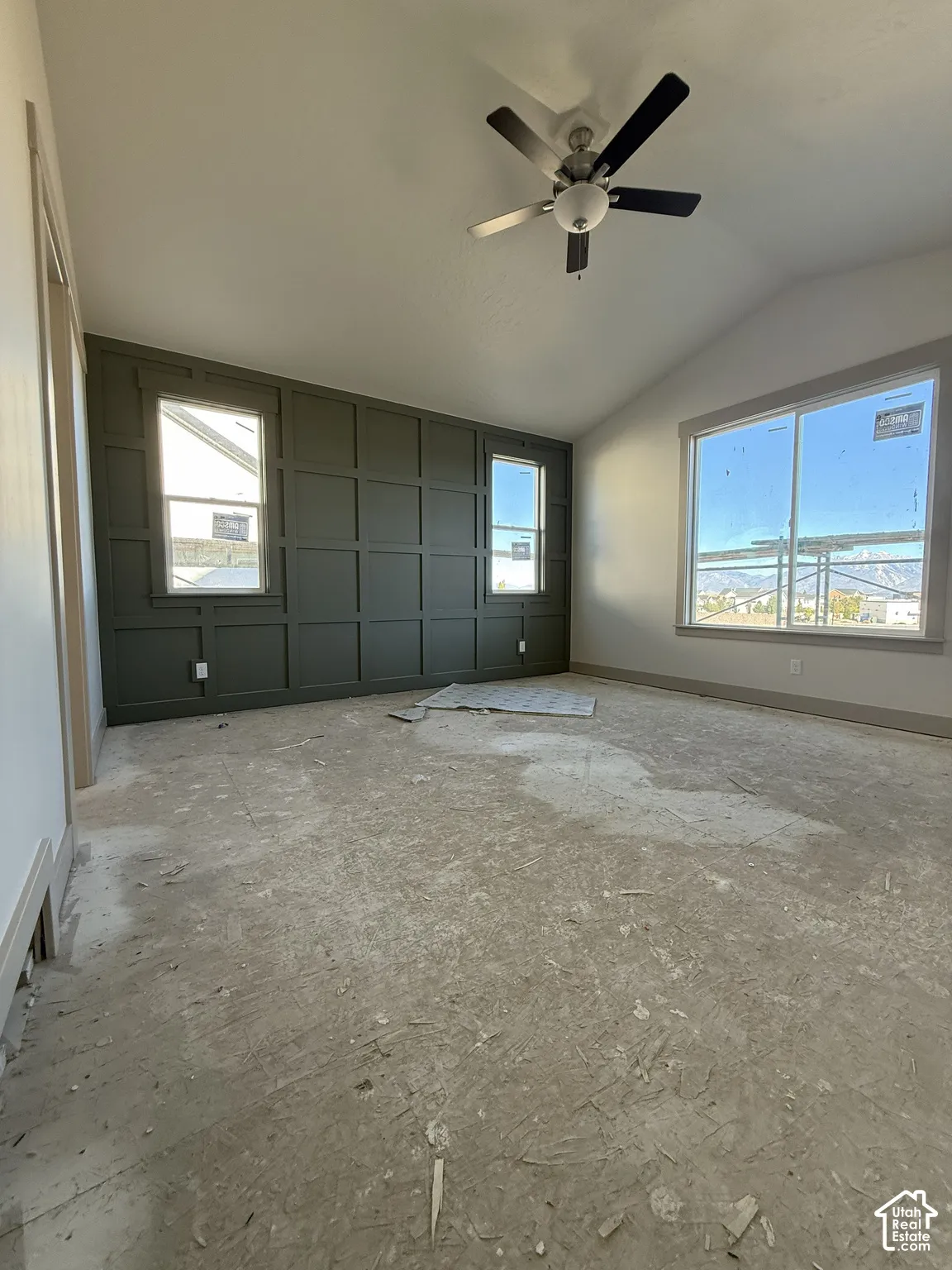 Vaulted ceilings featuring a central ceiling fan, an accent wall with grid-style millwork, and large windows