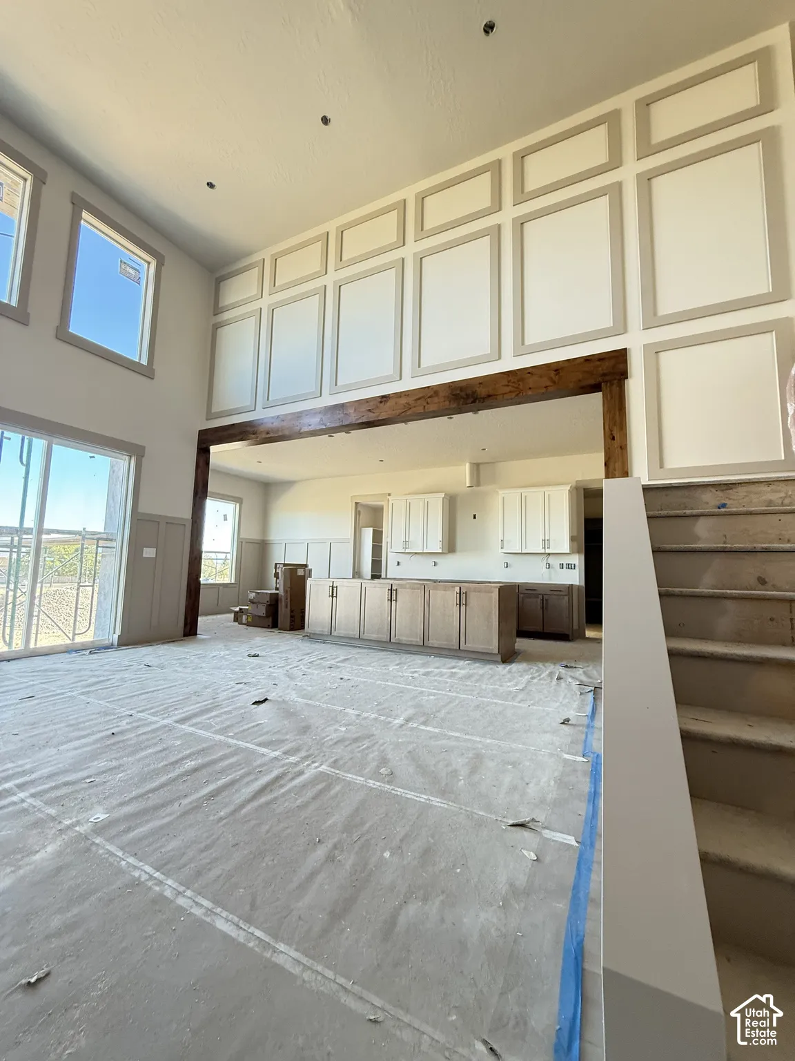 Double-height ceilings featuring decorative wall molding, exposed wood beam header, oversized windows, and built-in kitchen cabinetry