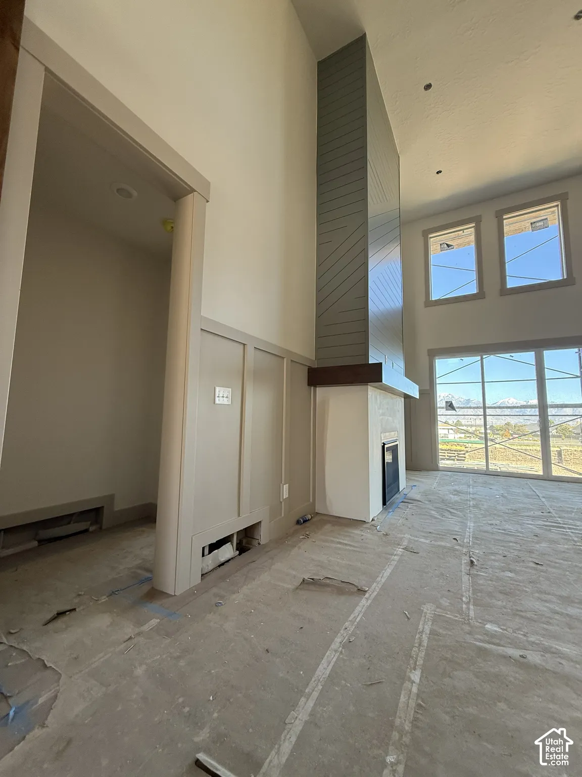 Double-height ceilings, floor-to-ceiling fireplace with decorative horizontal paneling, heavy timber mantel, custom wall molding, and expansive multi-pane windows