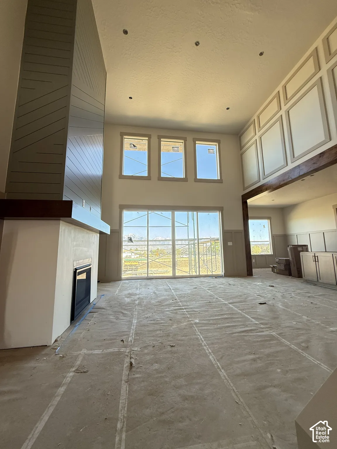 Double-height ceiling, floor-to-ceiling fireplace with decorative shiplap detailing, custom wall paneling, recessed lighting, and expansive windows