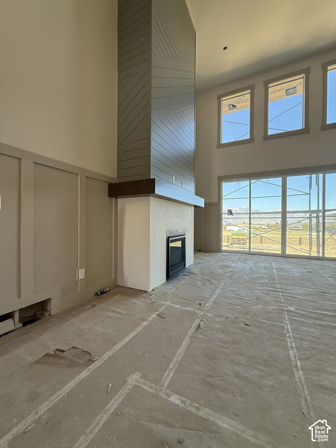 Full-height fireplace surround with geometric detailing and wood mantel, expansive windows, wall paneling, and high ceilings