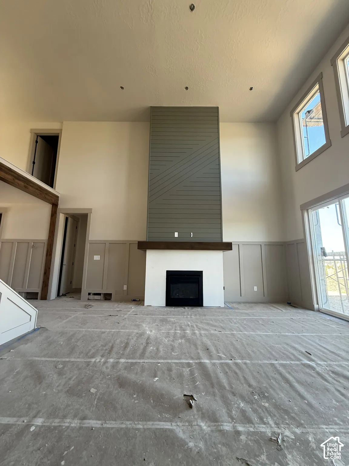 Two-story living area featuring a fireplace with a geometric-patterned surround, a thick wood mantel, wainscoting, and multi-paned windows
