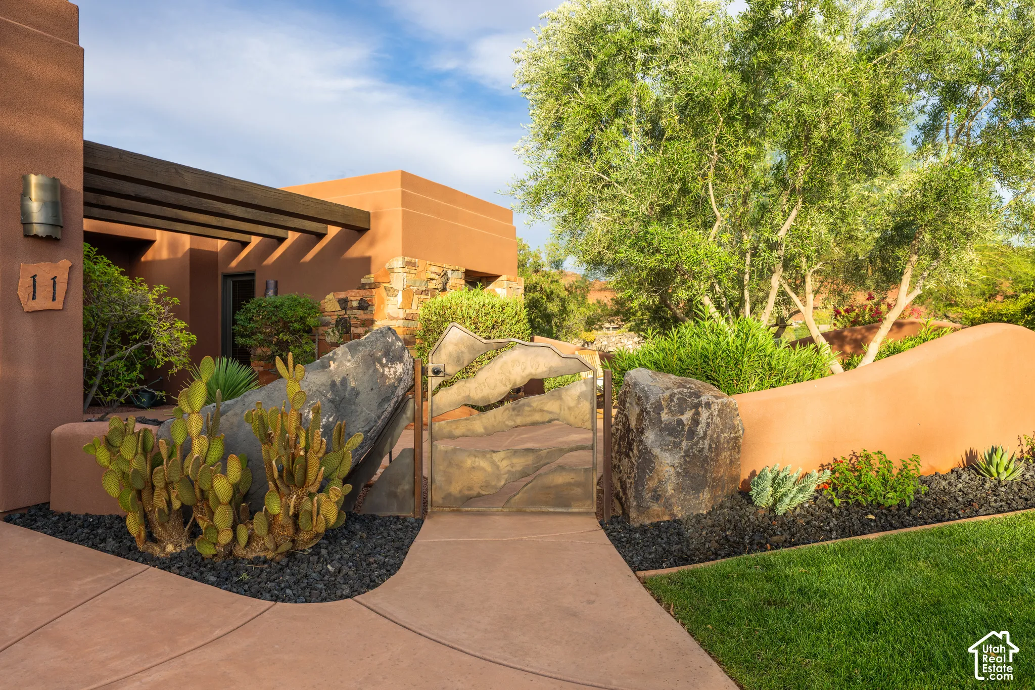 Stucco exterior with a wood pergola, custom metal gate, and rock landscaping